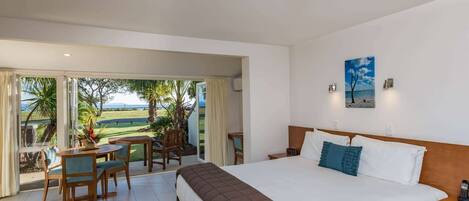 A bedroom with a large bed, a view of the outdoors, and a dining area with chairs and a table.