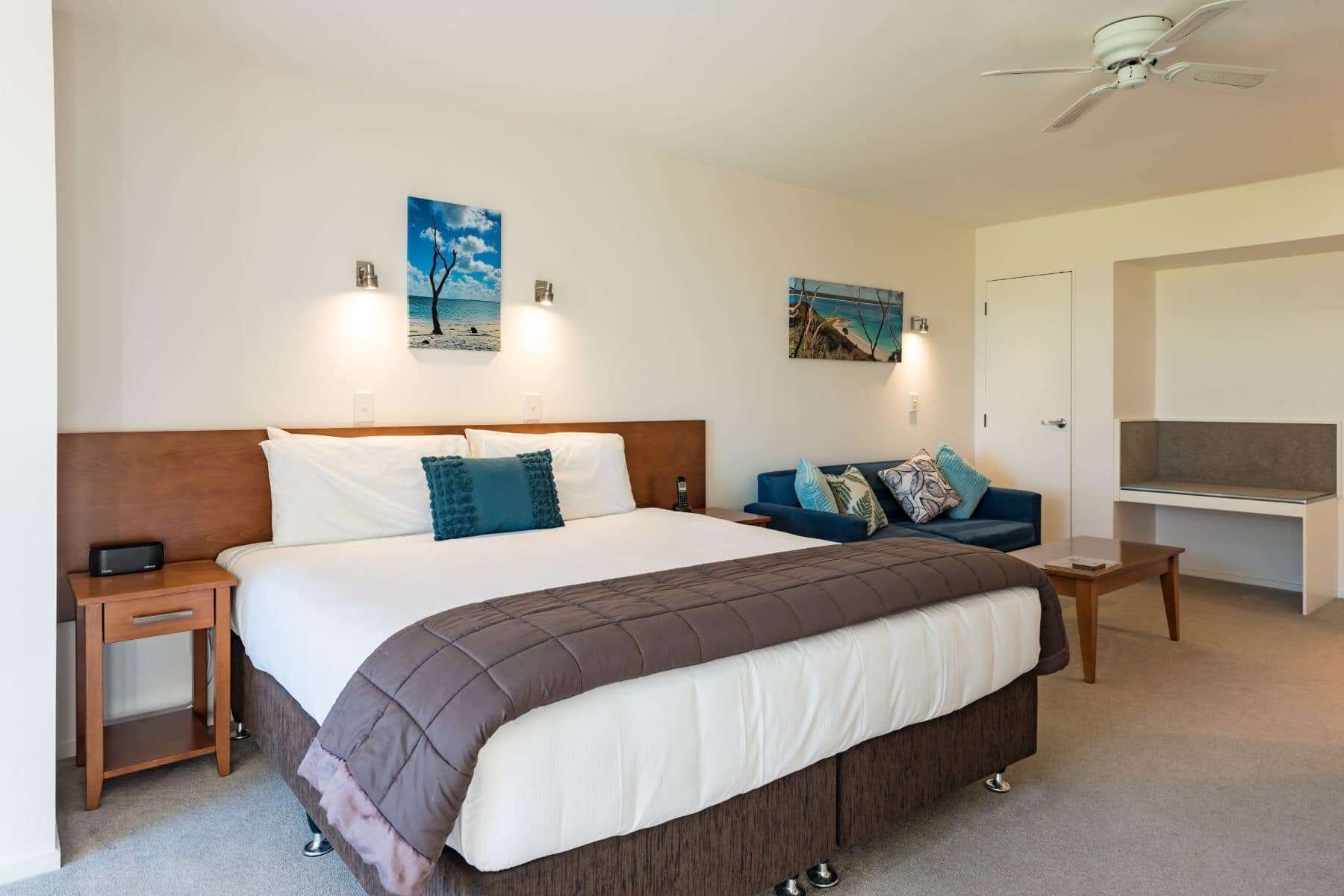 A bedroom with a large bed, a bedside table, a nightstand, a sofa, and two wall-mounted lamps.
