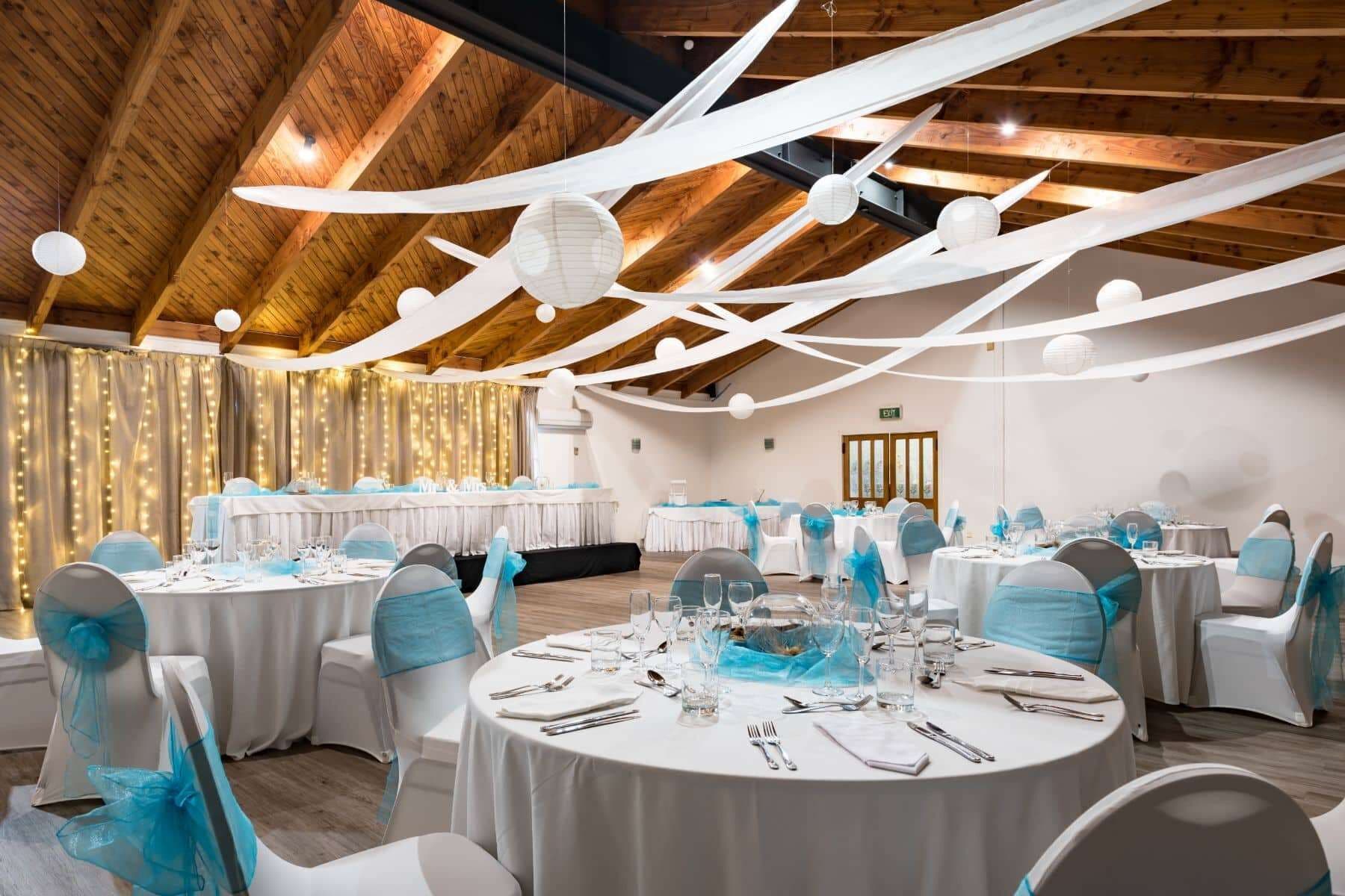 A banquet hall with round tables set for a formal event, featuring white tablecloths and blue chair covers.