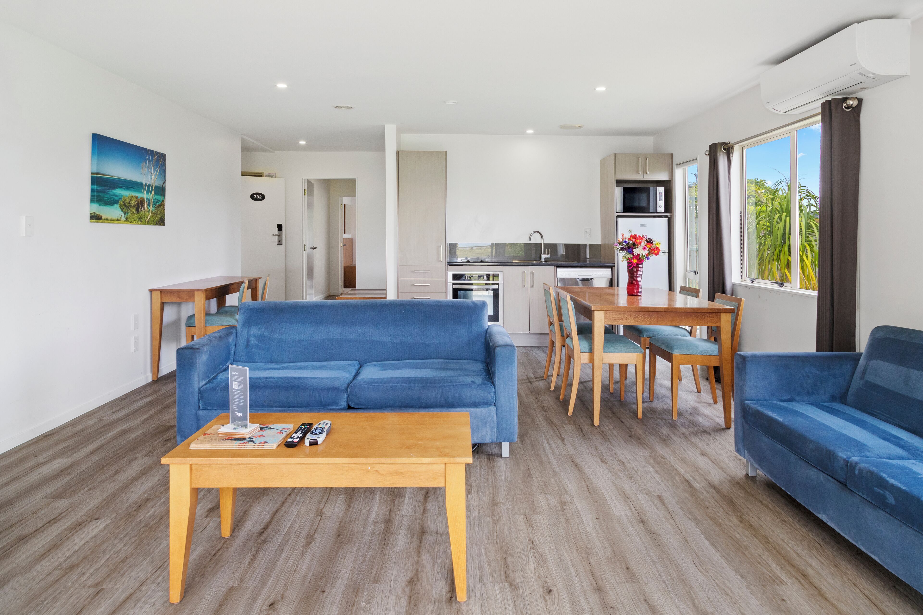 A modern living room with a blue sofa, wooden coffee table, and a dining area with a wooden table and chairs.