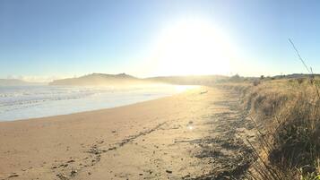 A beach with a clear sky and the sun low on the horizon.