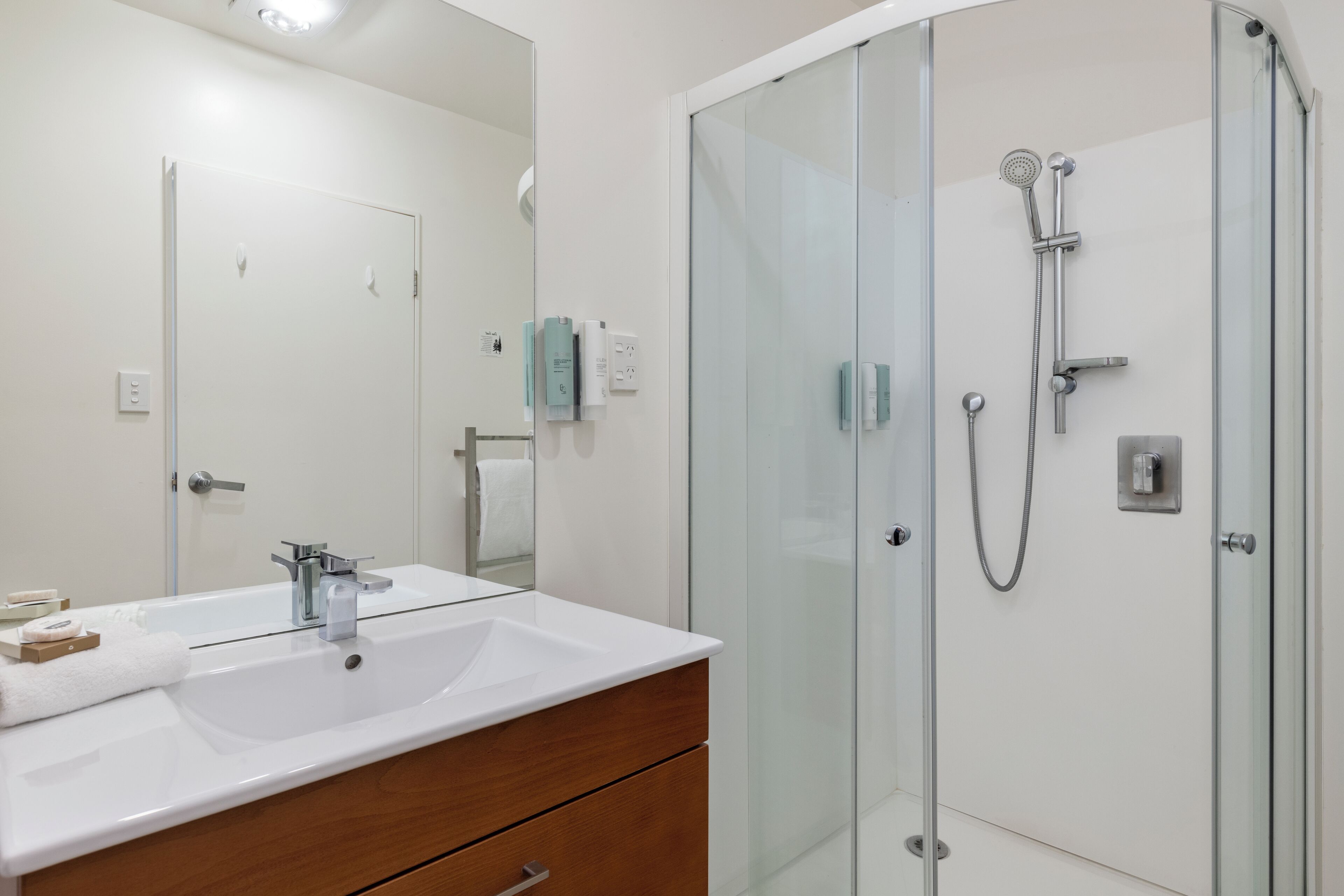 A modern bathroom with a white sink, wooden vanity, and a glass-enclosed shower area.