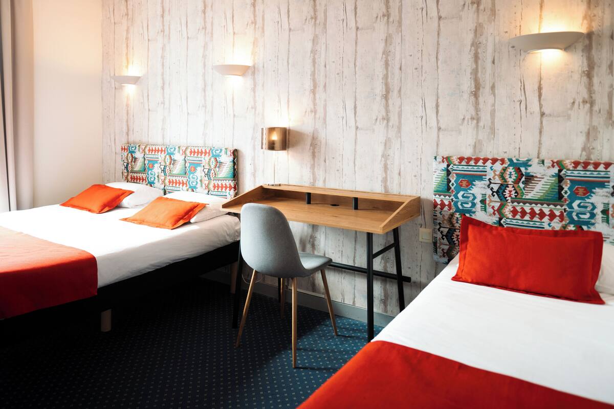 A hotel room with two beds, a desk, and a chair.
