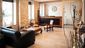 A hotel lobby with a reception desk, leather sofas, wooden coffee table, and a large wall clock. - Hotel Bellevue (Brest)