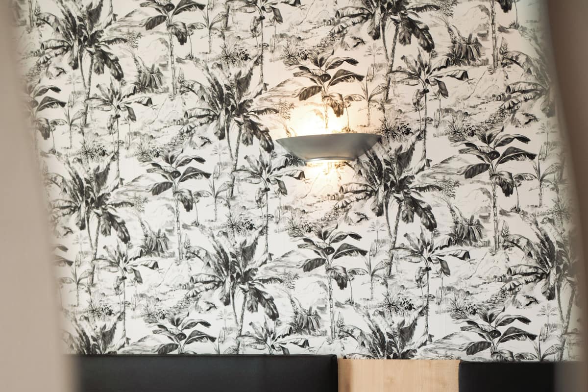 A hotel room with two beds, each with red and white bedding, and a wall with a tropical plant wallpaper.