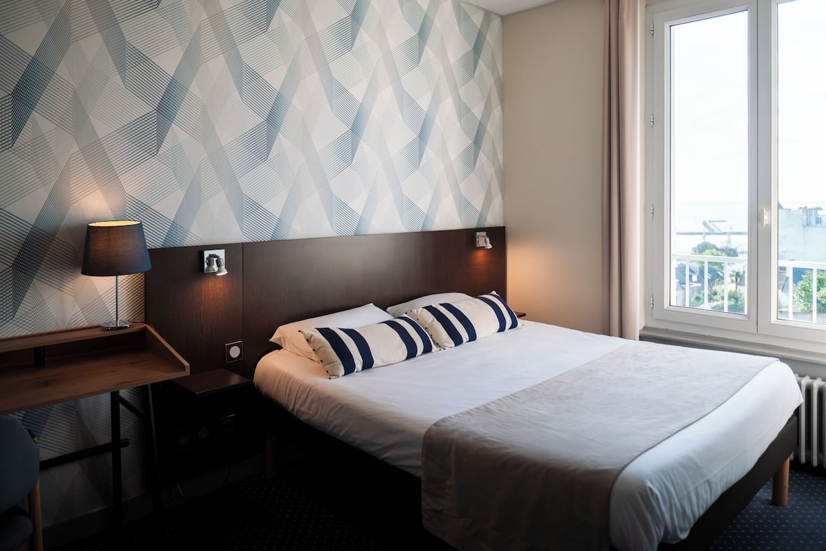 A hotel room with a bed, a desk, a lamp, and a window with a view.