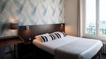 A hotel room with a bed, a desk, a lamp, and a window with a view.
