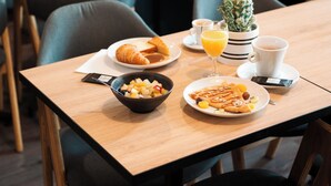 A dining table with breakfast items including croissants, a bowl of fruit, and a cup of coffee. - Hotel Bellevue (Brest)