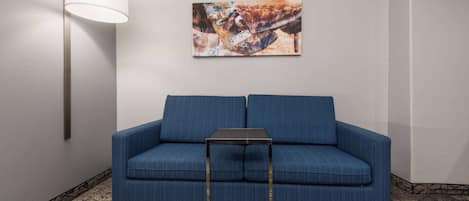 A blue sofa with a small table in front, a wall-mounted lamp, and a painting on the wall.