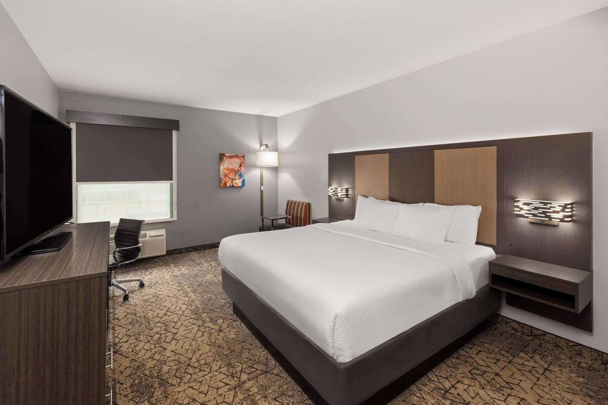 Une chambre d’hôtel avec un grand lit, un bureau doté d’un téléviseur à écran plat, une chaise, une lampe et un luminaire fixé au mur.