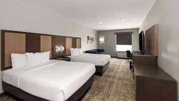 Une chambre d’hôtel avec deux lits, un bureau, une télévision et une salle de bain que l’on aperçoit à l’arrière-plan.