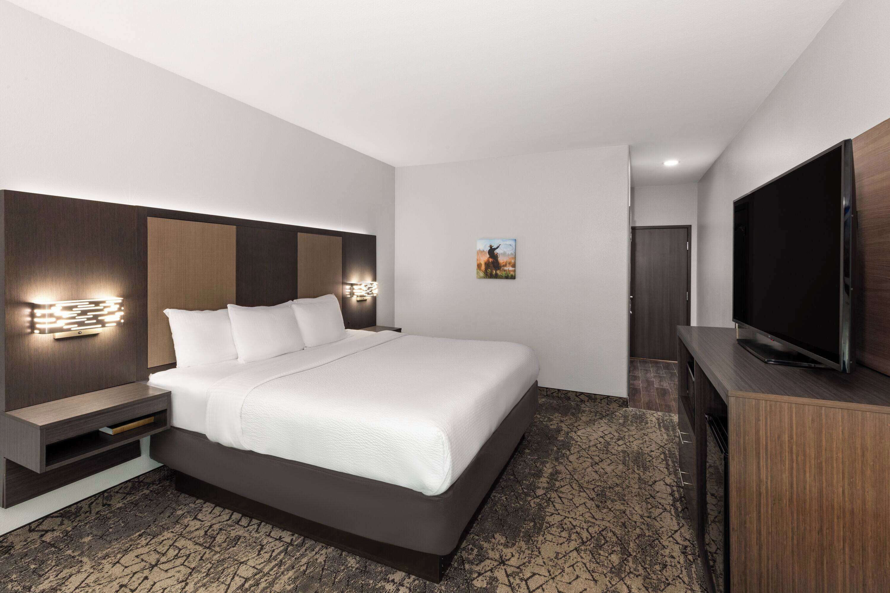 A modern hotel room with a large bed, built-in TV, and a small seating area.