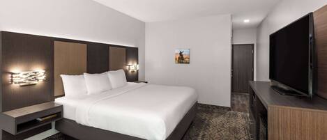 A modern hotel room with a large bed, built-in TV, and a small seating area.