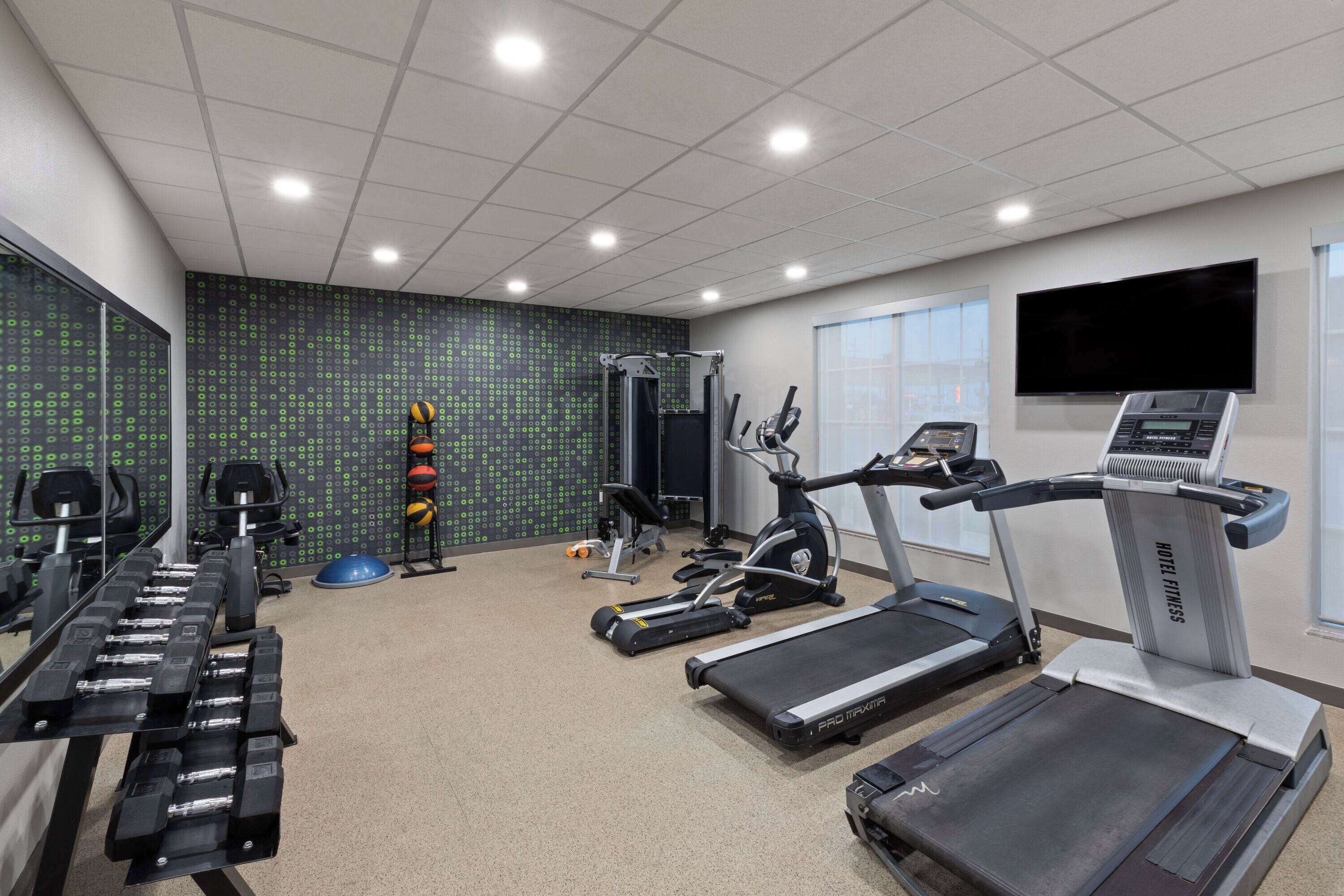 A hotel fitness center with treadmills, elliptical machines, and free weights.
