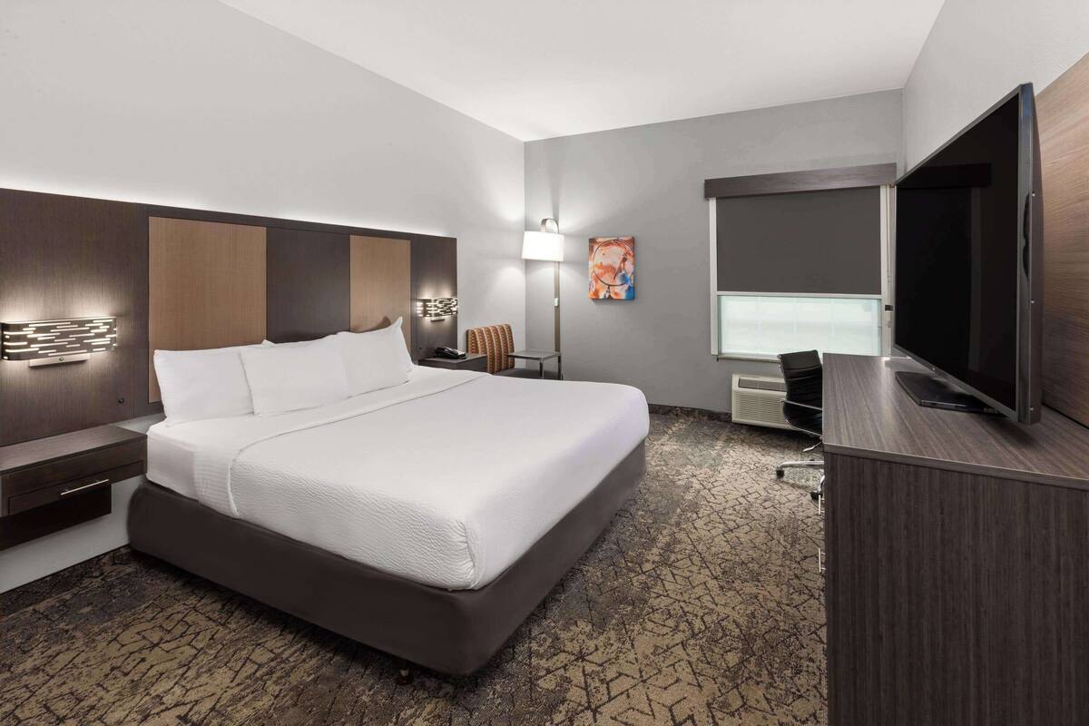 Une chambre d’hôtel avec un grand lit, un bureau doté d’un téléviseur à écran plat, une lampe et un tableau au mur.