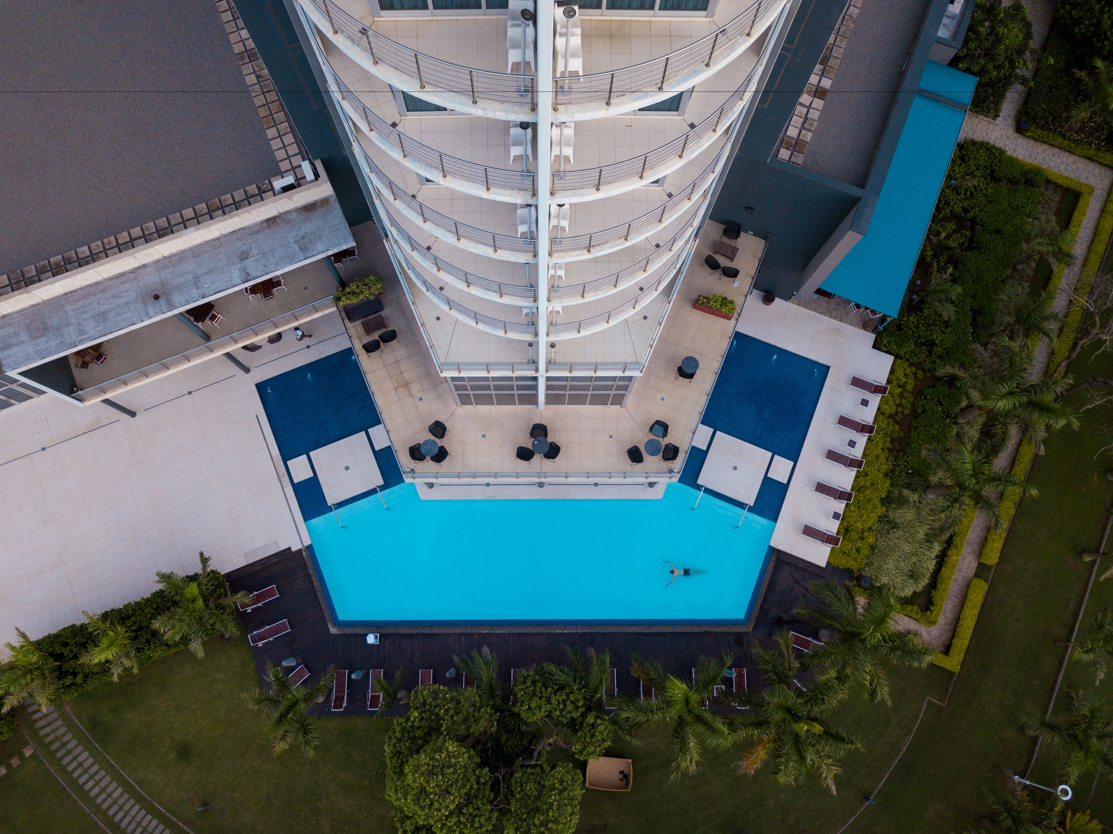 Un hôtel à plusieurs étages doté d’un atrium central, d’une piscine extérieure et entouré de verdure.
