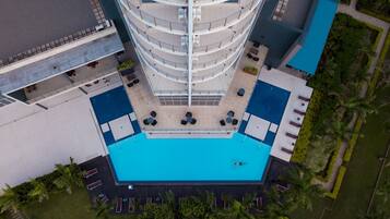 Un hôtel à plusieurs étages doté d’un atrium central, d’une piscine extérieure et entouré de verdure.