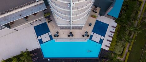 Un hotel de varios pisos con un atrio central, piscina exterior y zonas verdes circundantes.