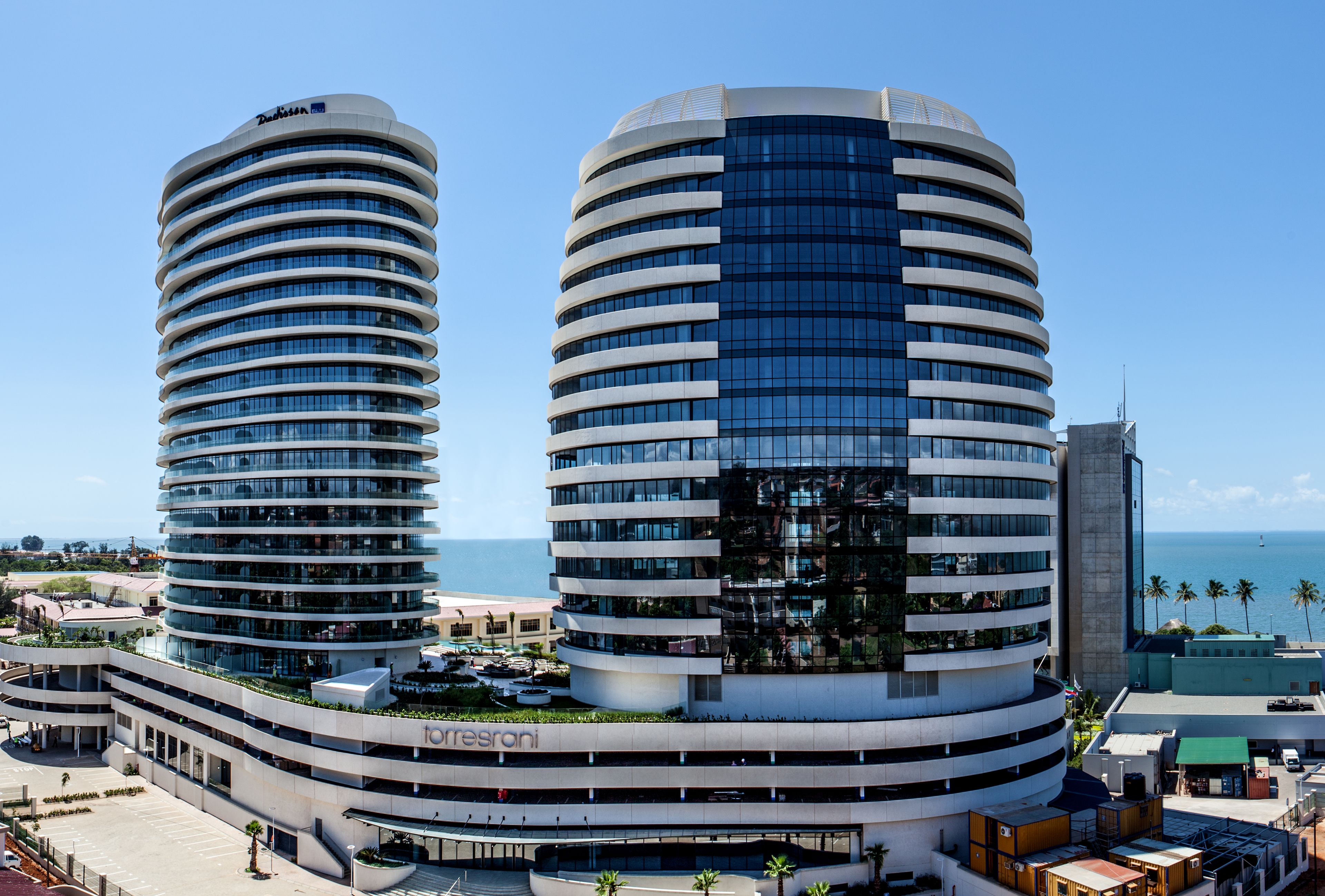 A modern hotel with a curved facade, multiple balconies, and a view of the sea.