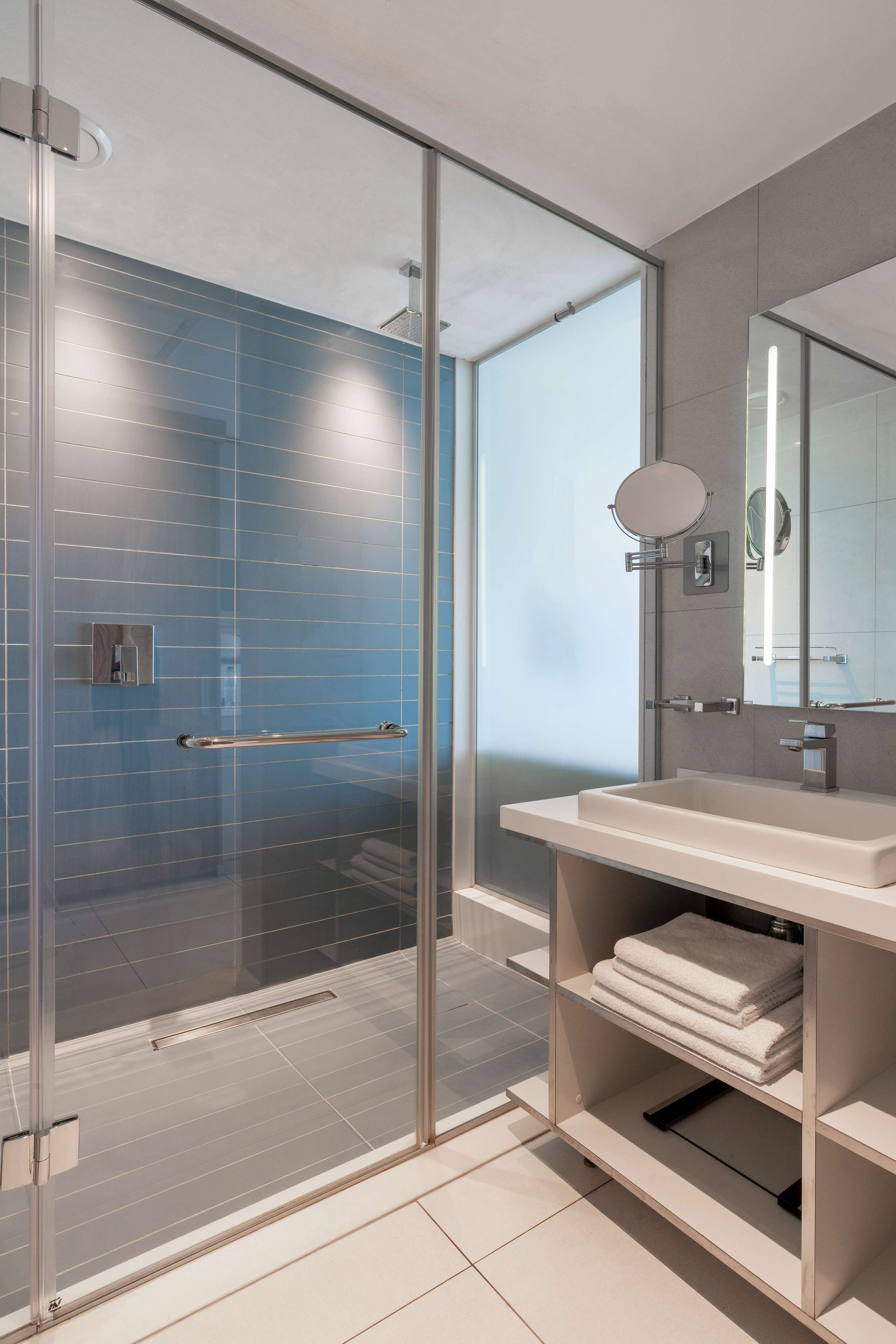 Un baño moderno con cabina de ducha de vidrio, un lavabo blanco y un espejo.