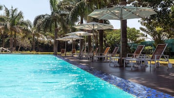 Relax by the serene pool surrounded by palm trees and lounge chairs.
