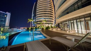 A modern hotel with a pool, lounge chairs, and a distinctive curved building in the background. - Radisson Blu Hotel & Residence, Maputo (Maputo)