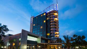 A modern hotel with a curved facade, multiple balconies, and a pool area.