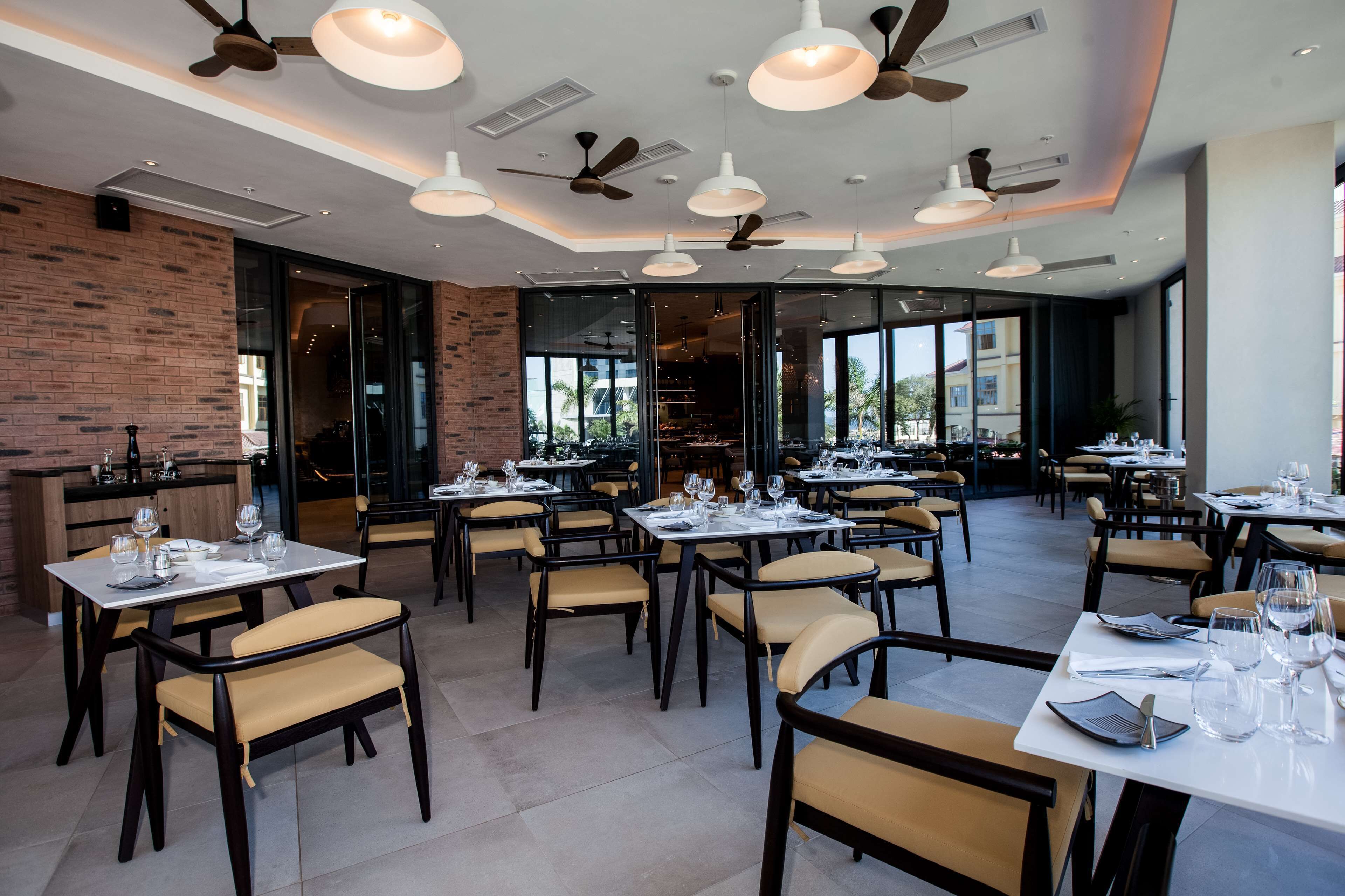 A restaurant with multiple tables and chairs, ceiling fans, and large windows offering a view of the outside.