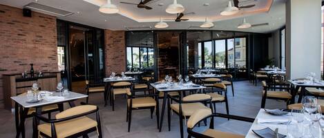 A restaurant with multiple tables and chairs, ceiling fans, and large windows offering a view of the outside.