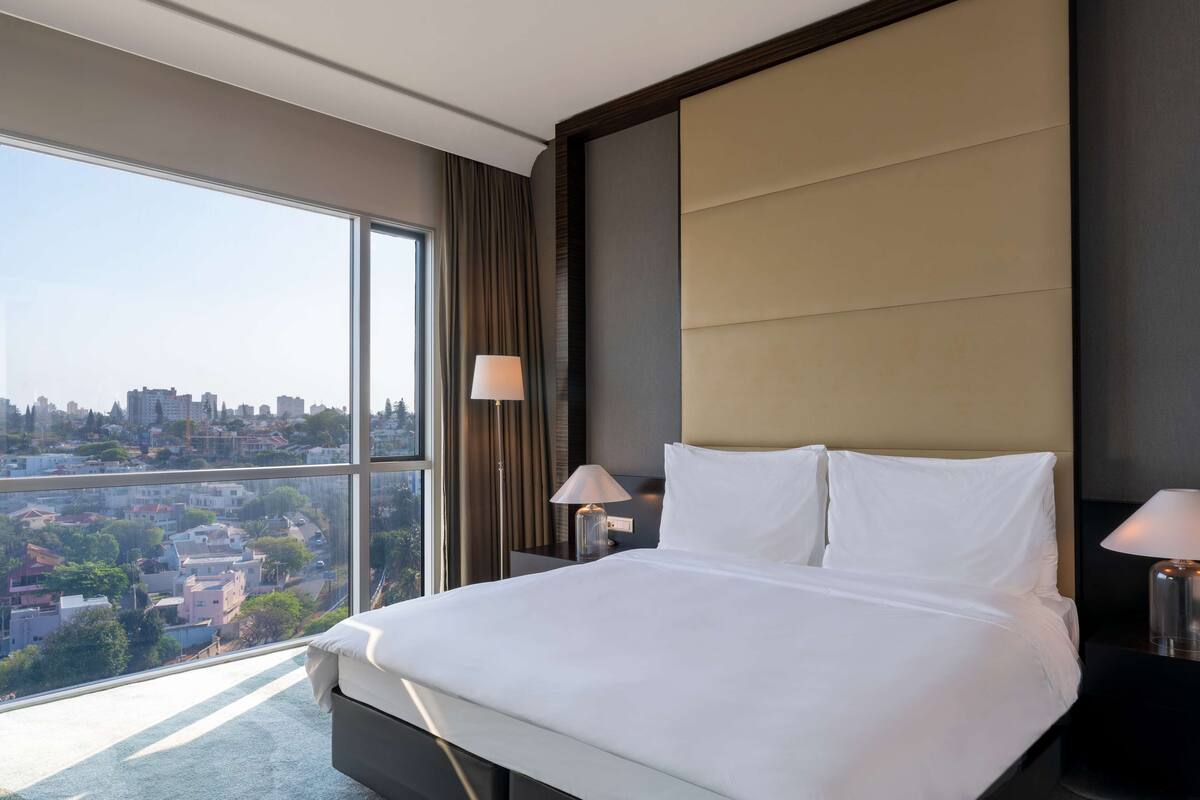 A hotel room with a large window, a bed, two bedside lamps, and a city view.