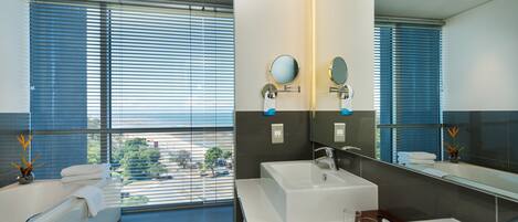 A modern bathroom with a large window, a bathtub, and two sinks.