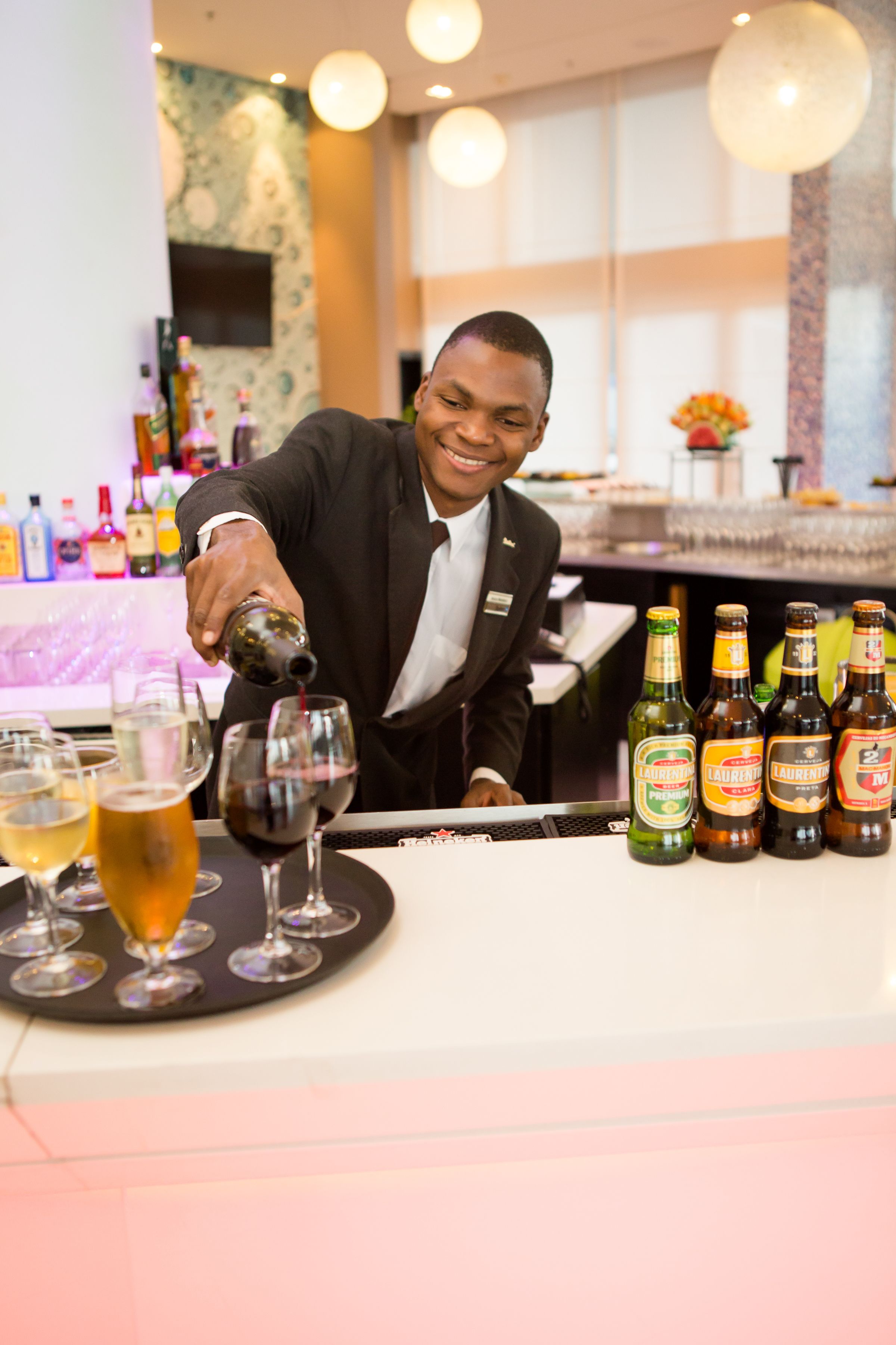 Um bartender a servir uma bebida num copo. Há garrafas de cerveja e vinho no balcão.