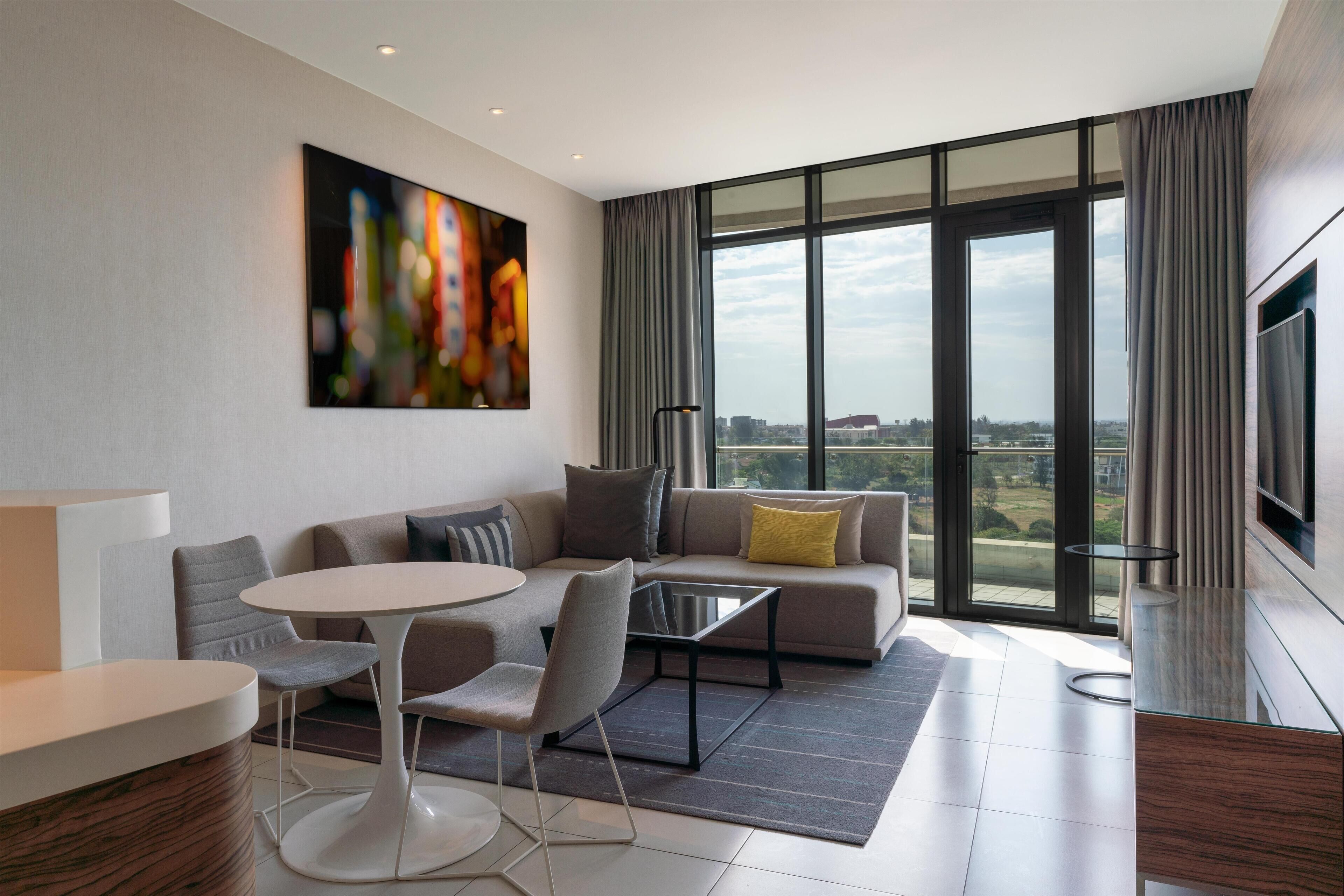 Una sala de estar moderna con sofá, sillones, una mesa de centro y un amplio ventanal con vistas a la ciudad.