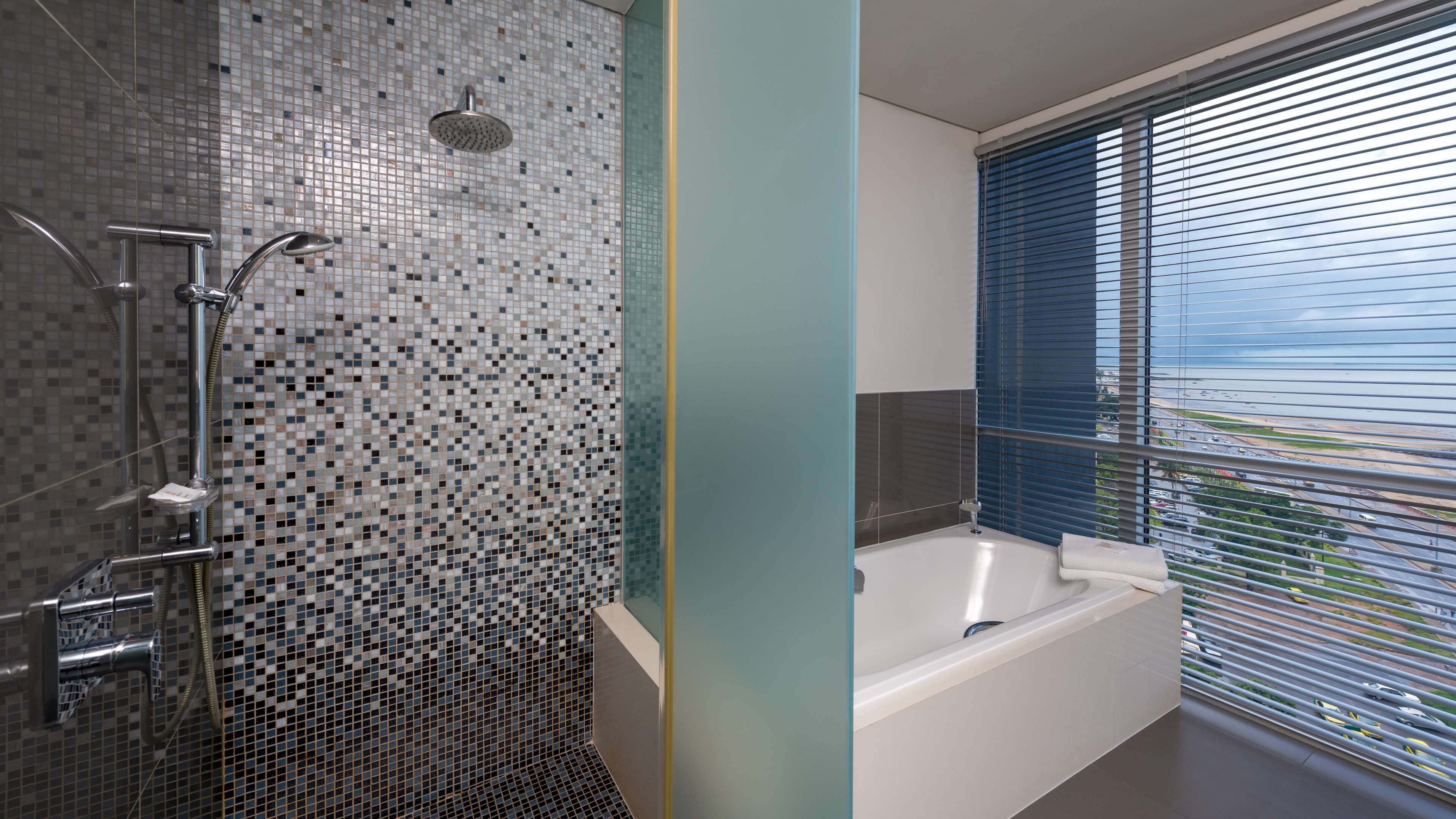 Ein Badezimmer mit Dusche, Badewanne und einem Fenster mit Jalousien.