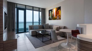 A modern living room with a sofa, coffee table, and chairs, a TV, and a large window with a view of the sea. - Radisson Blu Hotel & Residence, Maputo (Maputo)