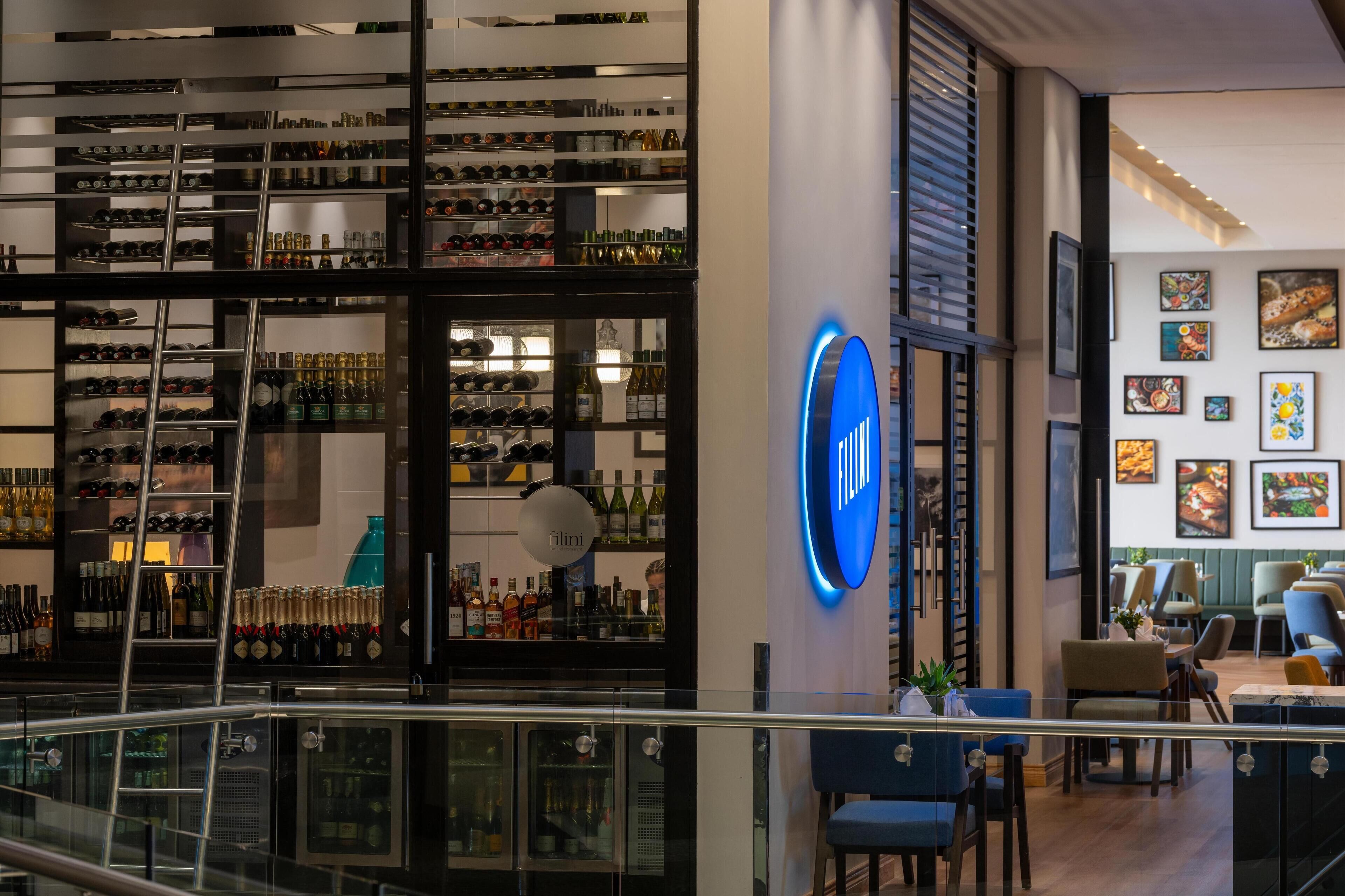 Un espace bar moderne avec des étagères remplies de bouteilles et un panneau lumineux au néon.