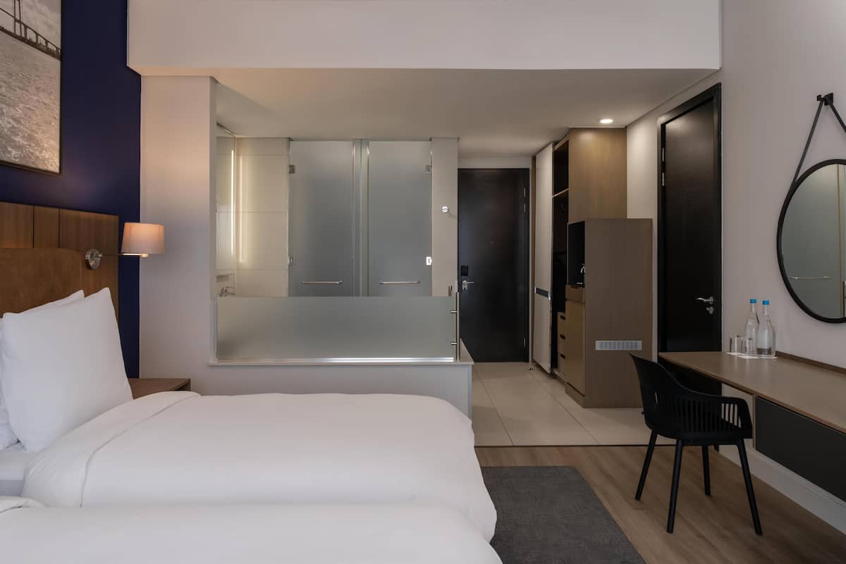 A modern hotel room with a large bed, a desk, a chair, a mirror, and a wardrobe.