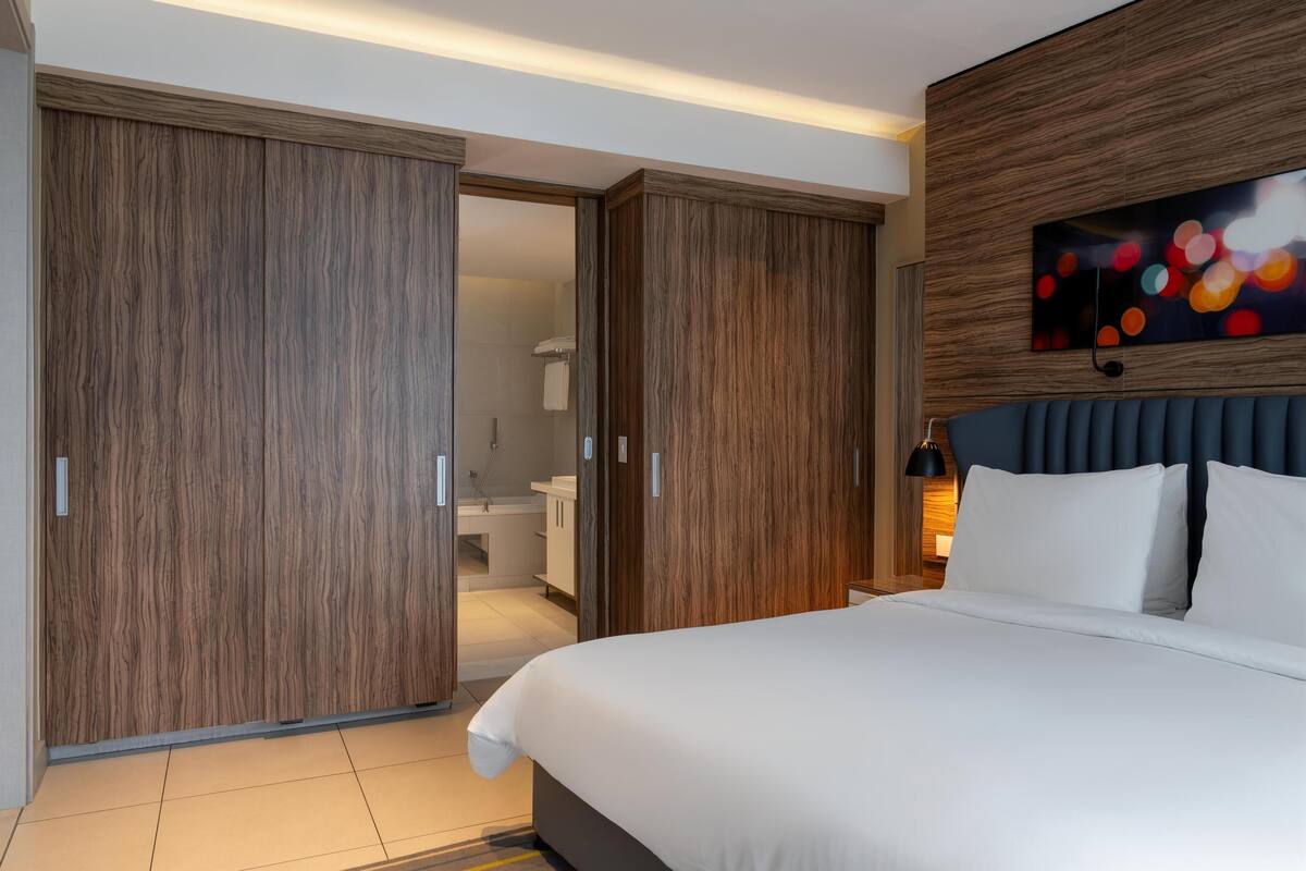 A hotel room with a large bed, wooden wardrobe, and a bathroom visible through the wardrobe doors.