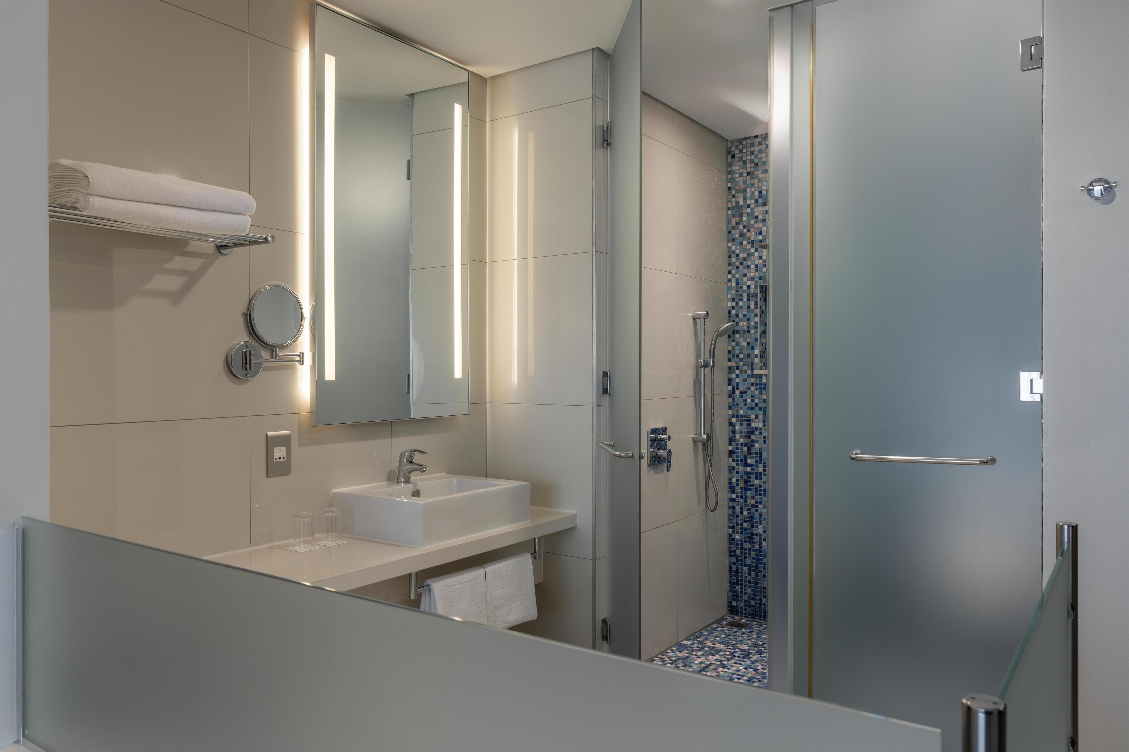A modern bathroom with a glass shower enclosure, a white sink, and a large mirror.