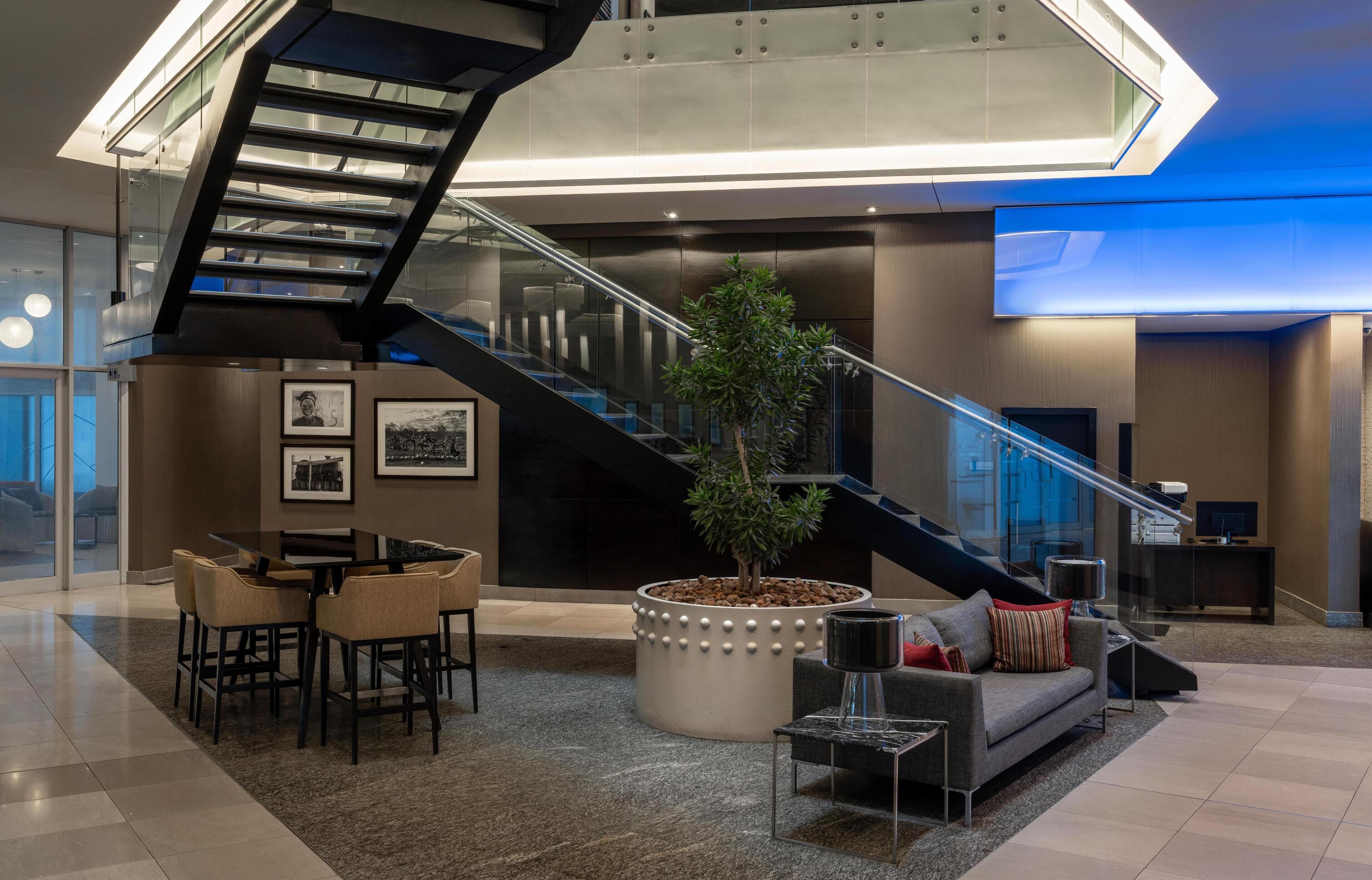 Un lobby moderno con una escalera, una zona de estar y una planta en maceta.