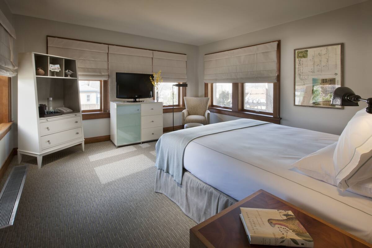 A hotel room with a bed, a desk, a chair, a TV, and a wardrobe.