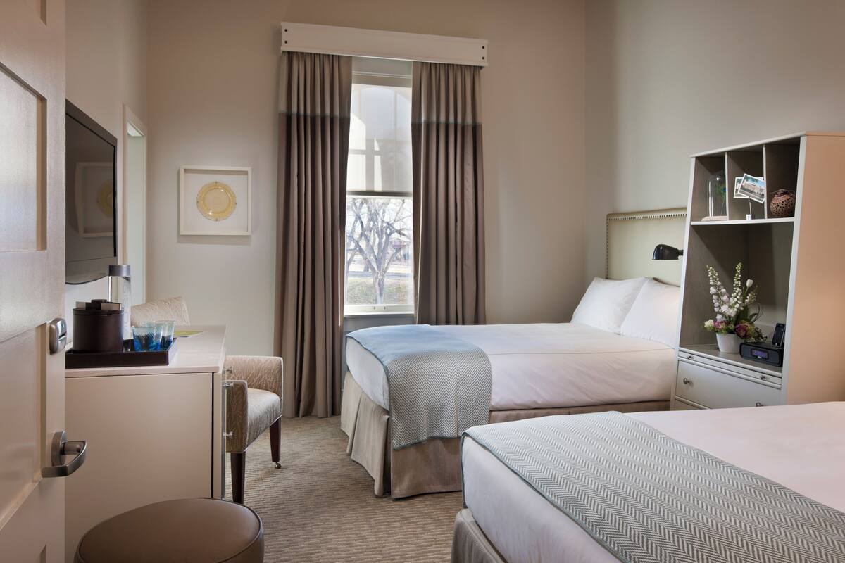 A hotel room with two beds, a desk, a chair, a wardrobe, and a window with curtains.