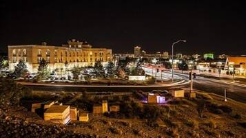 Une vue nocturne d’une ville, avec ses bâtiments illuminés, un rond-point et un chantier de construction où se dressent des structures temporaires.
