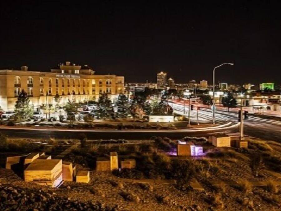 Une vue nocturne d’une ville, avec ses bâtiments illuminés, un rond-point et un chantier de construction où se dressent des structures temporaires.
