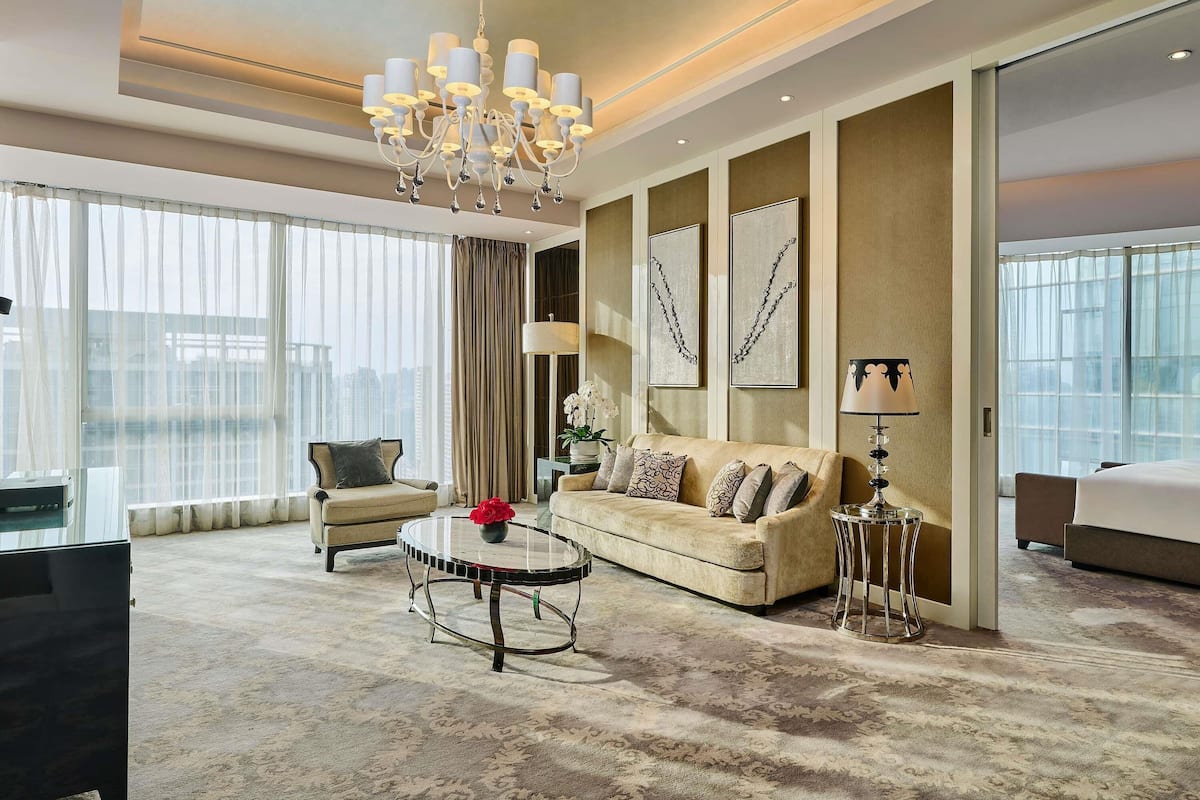 A spacious hotel room with a large bed, a sofa, a round coffee table, and a chandelier.
