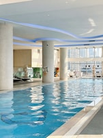 Una piscina interna con acqua cristallina, circondata da ampie finestre che offrono vista sulla città.