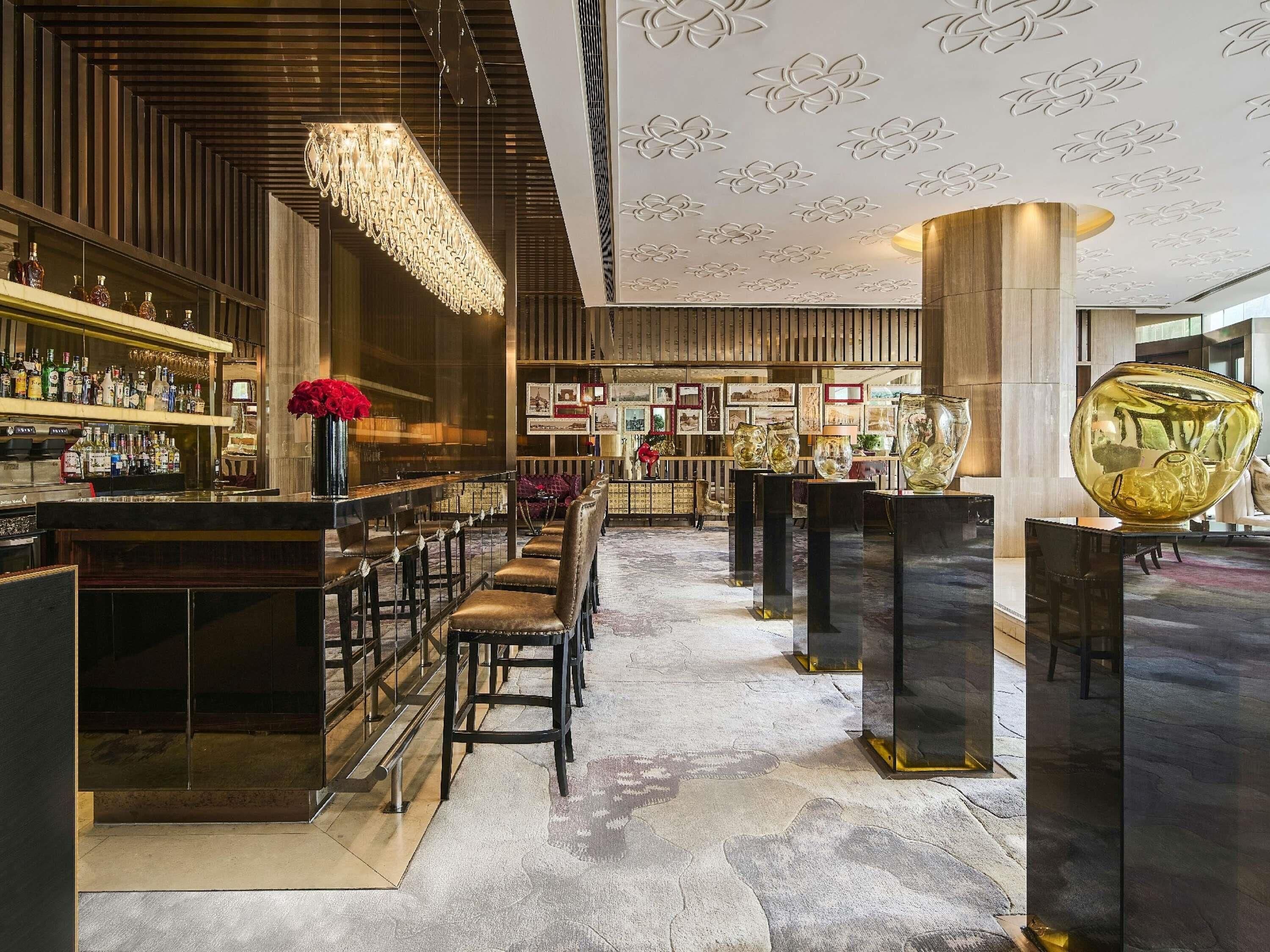 A bar area with a long counter, bar stools, and a variety of bottles.