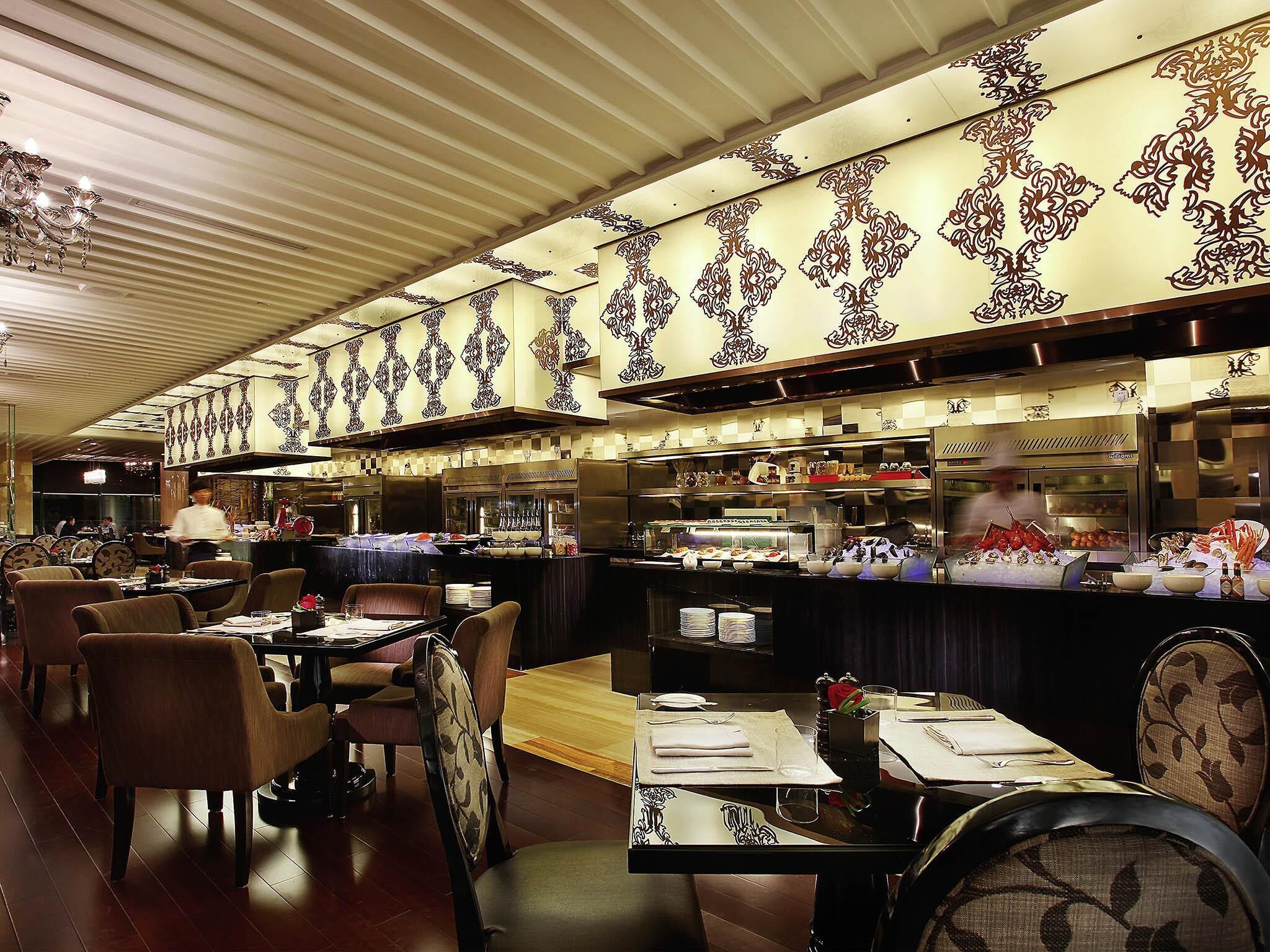 Interior de un restaurante con mesas, sillas, una barra y un chef al fondo.