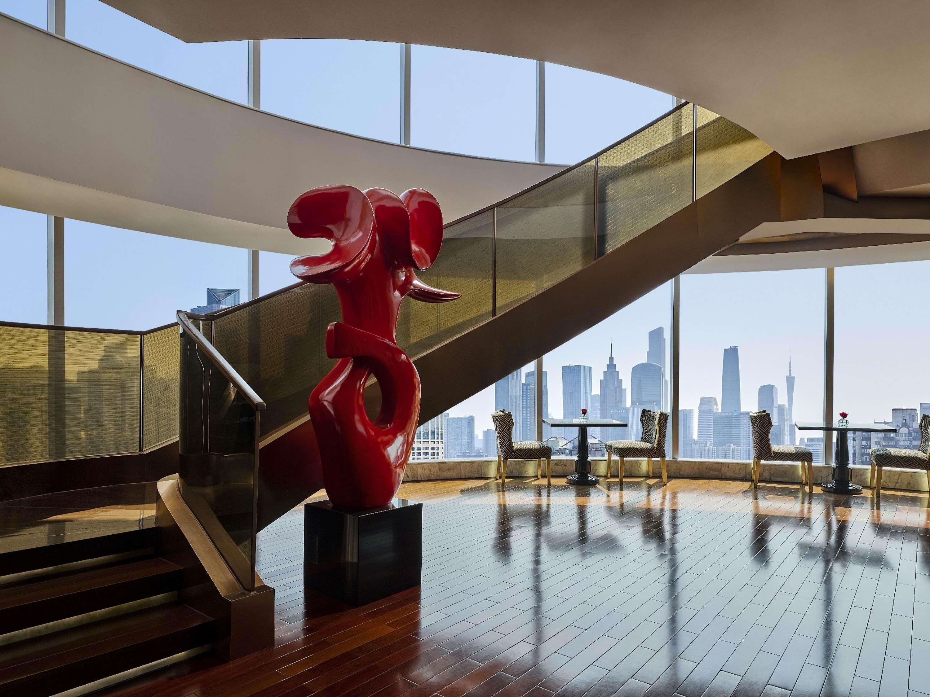 A modern interior with a staircase, a red sculpture, and a city skyline view.