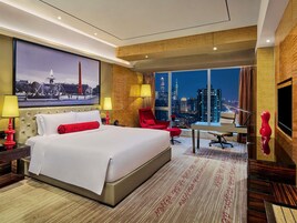 Camera d'albergo con un letto grande, una scrivania, una sedia, una televisione e vista sulla città.